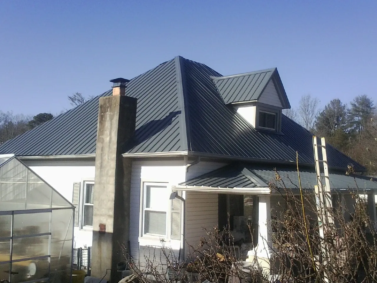 Dark blue standing seam metal roof on a white farmhouse with dormer — Slate & Tile Roof Repair by Roofing Brothers in Richmond